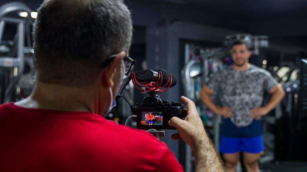 Mann posiert für die Kamera, während Vlogger im Fitnessstudio filmt
