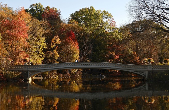 Menschen gehen bei Sonnenaufgang im Central Park über die Bow Bridge