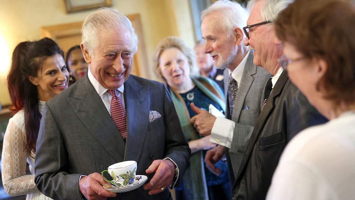 König Charles lächelte, während er eine Tasse und eine Untertasse in der Hand hielt