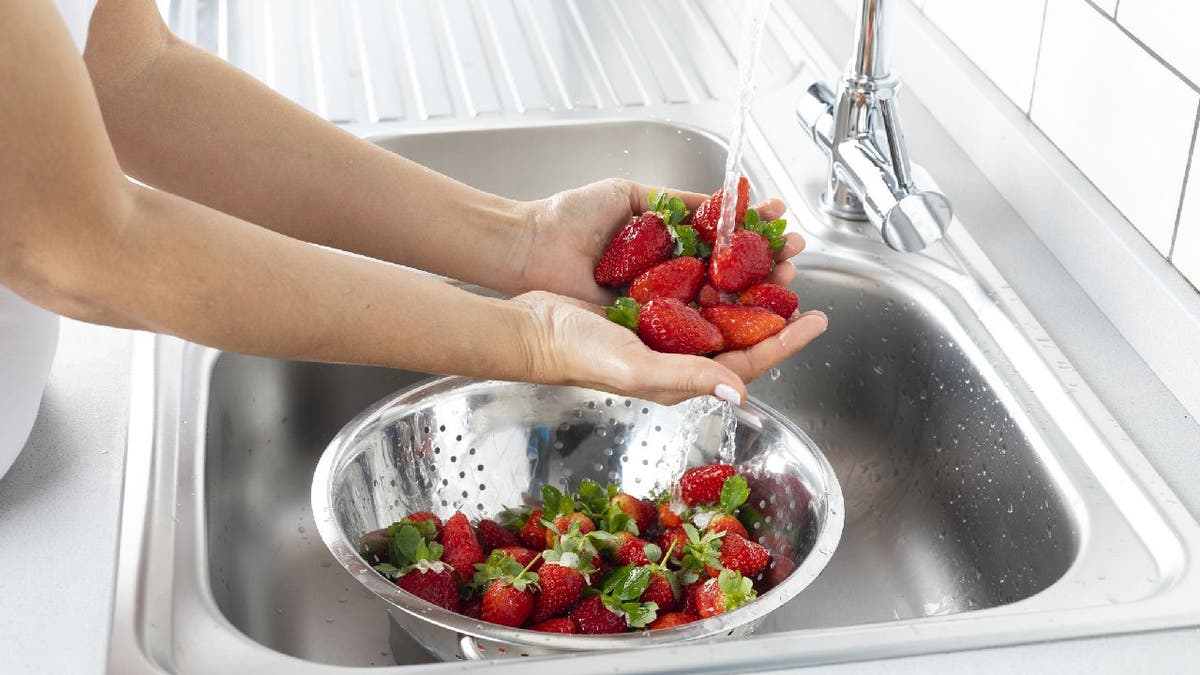 Frau wäscht Erdbeeren in einem Spülbecken.