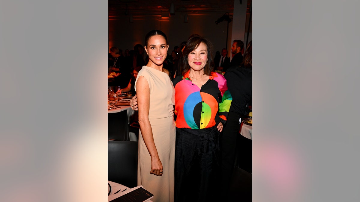 Meghan Markle trägt ein beiges Kleid und posiert neben Janet Yang in einer farbenfrohen Bluse