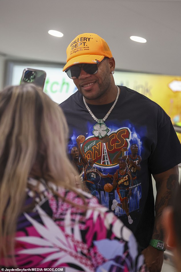 Low-Hitmacher Flo Rida sah gut aus in einem schwarzen Seattle Sonics-T-Shirt, einer orangefarbenen Baseballkappe und einer trendigen dunklen Sonnenbrille