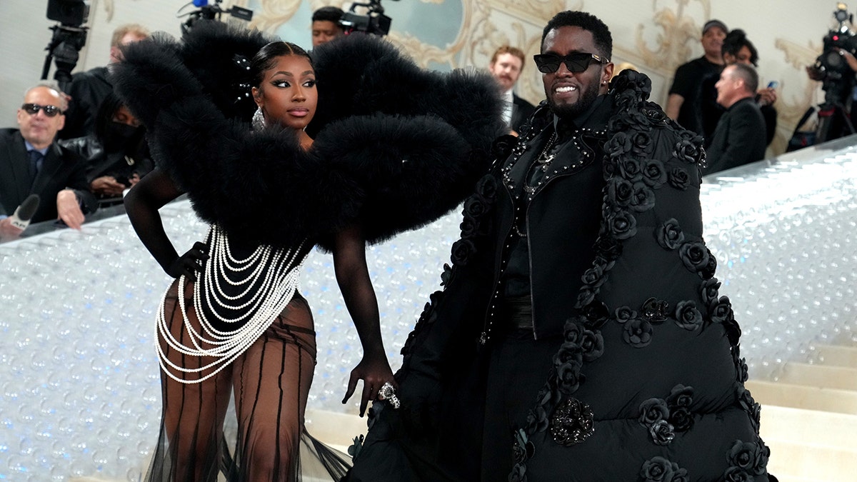 Yung Miami in einem Perlenkleid und einem dramatischen Federoberteil blickt Diddy auf dem Met Gala-Teppich an