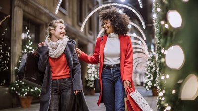 Hübsche junge Freundinnen lächeln breit und fröhlich, haben Spaß im Einkaufszentrum und kaufen Weihnachtsgeschenke
