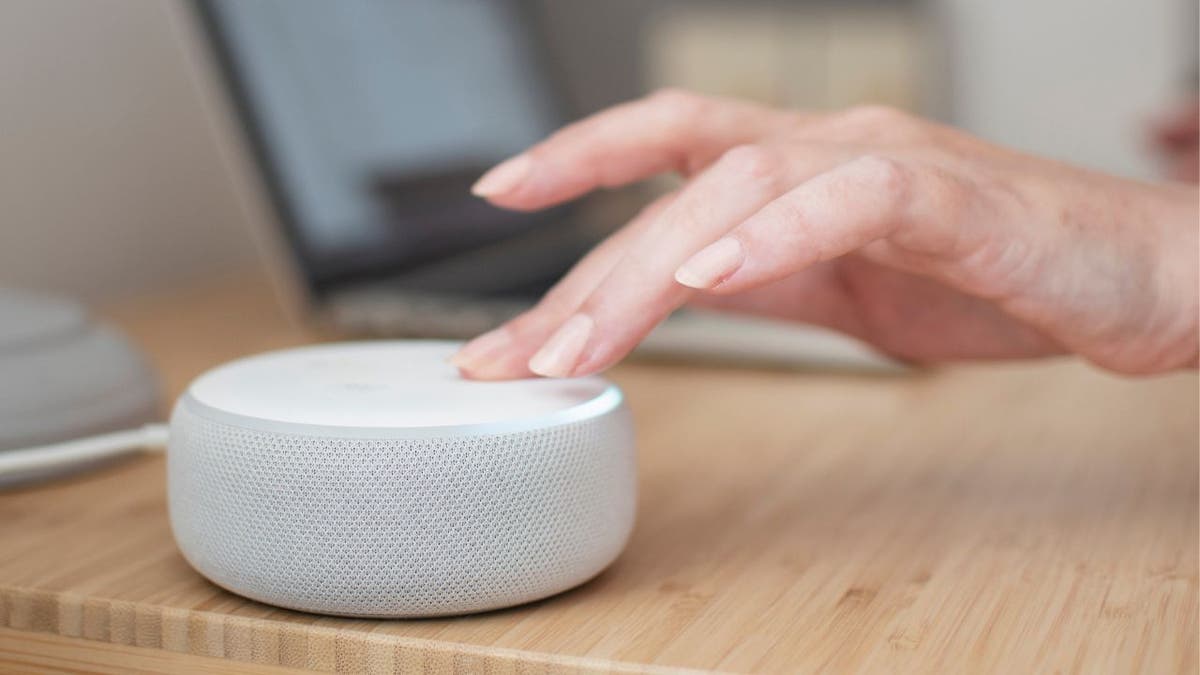 Weißes Amazon Echo-Gerät auf einem hellen Holztisch mit einer Hand, die das Gerät berührt