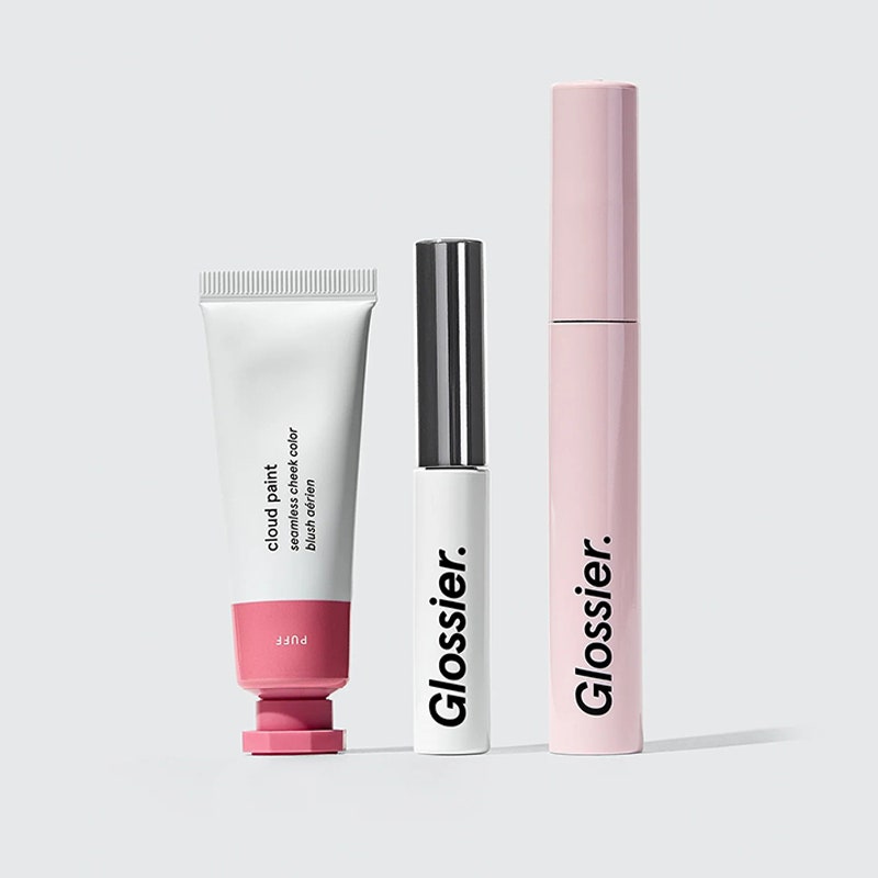 Das Glossier The Makeup Set aus Wolkenfarbtube, Boy Brow und rosa Mascara auf grauem Hintergrund