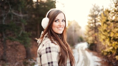 Glückliche Frau trägt Ohrenschützer, während sie im Winter auf dem Fußweg steht