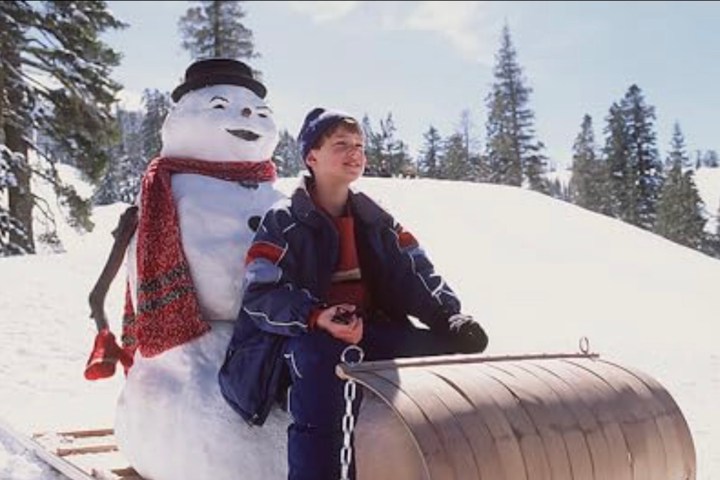 A boy goes down a hill on a sled with a snowman.