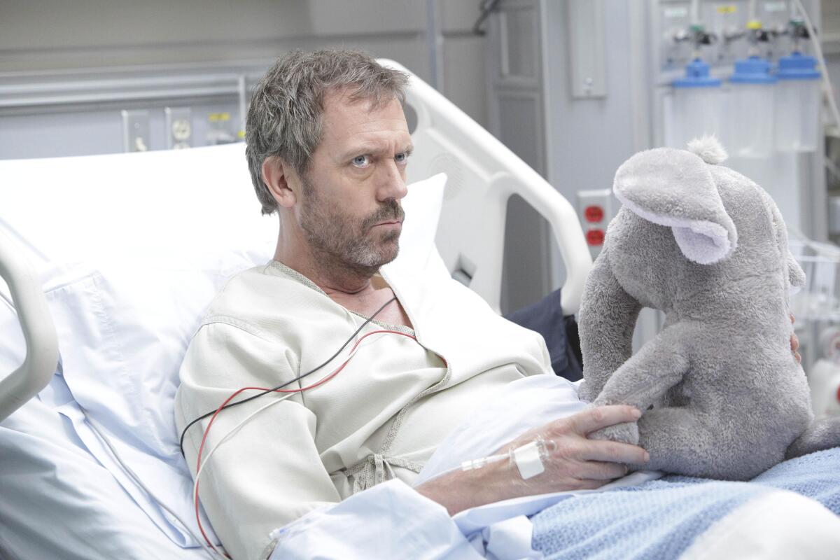 Ein mürrischer Mann in einem Krankenhausbett hält einen ausgestopften Elefanten.