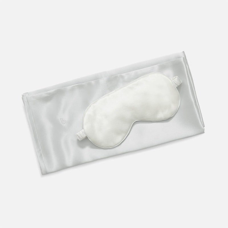 Brooklinen Mulberry Silk Bundle: Ein weißer Kissenbezug und eine passende Augenmaske auf grauem Hintergrund