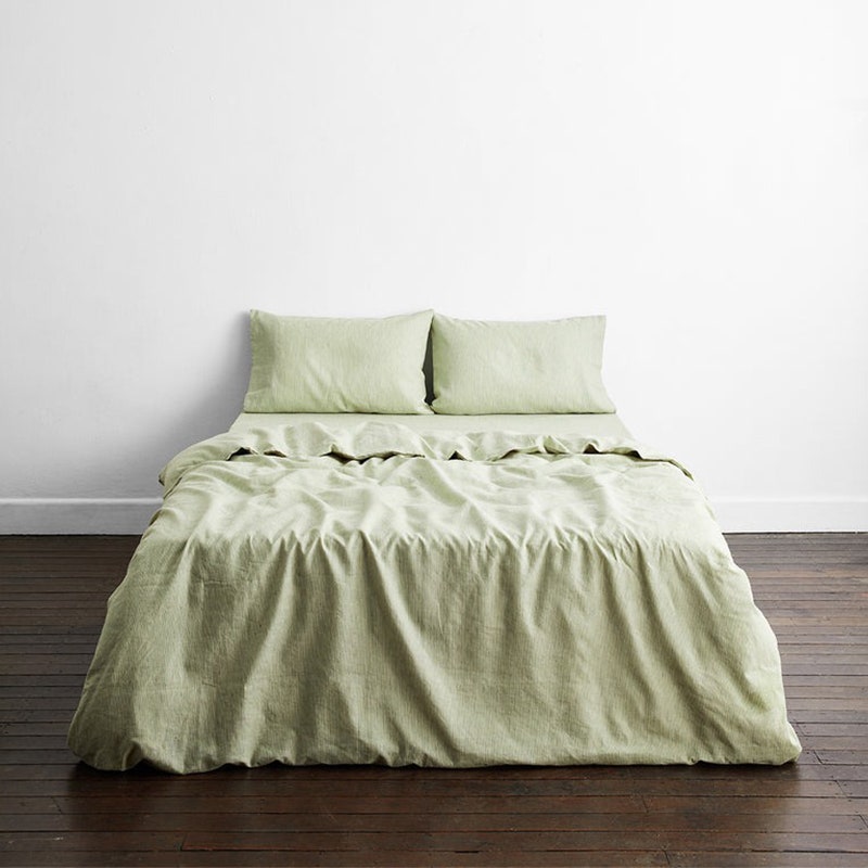 Bed Threads Bettwäscheset aus 100 % französischem Flachsleinen: Ein Bett mit grünen Laken in einem Zimmer mit dunkelbraunen Holzböden und weißen Wänden
