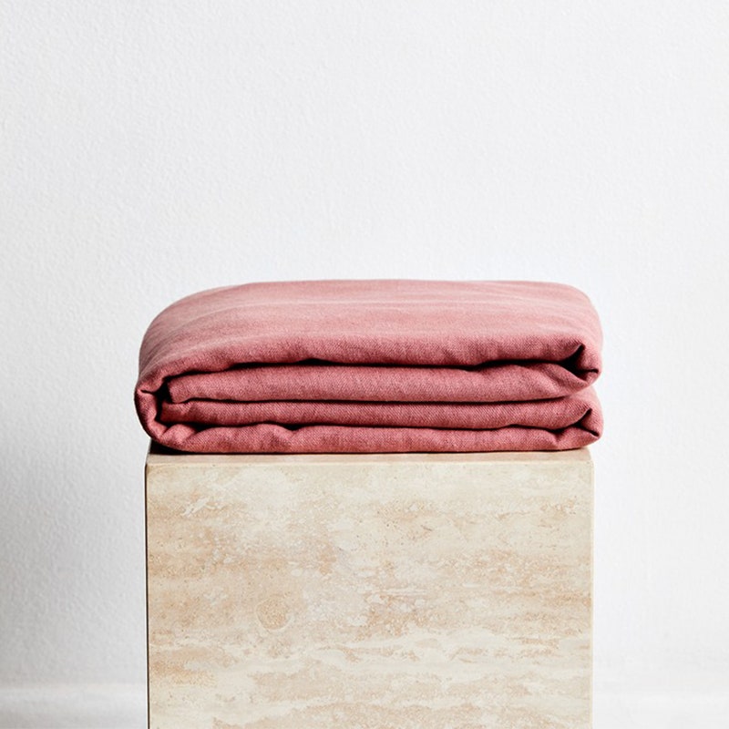 Bed Threads Überwurf aus 100 % französischem Flachsleinen: Eine rosa Überwurfdecke, gefaltet auf einer beigen Säule vor einer weißen Wand