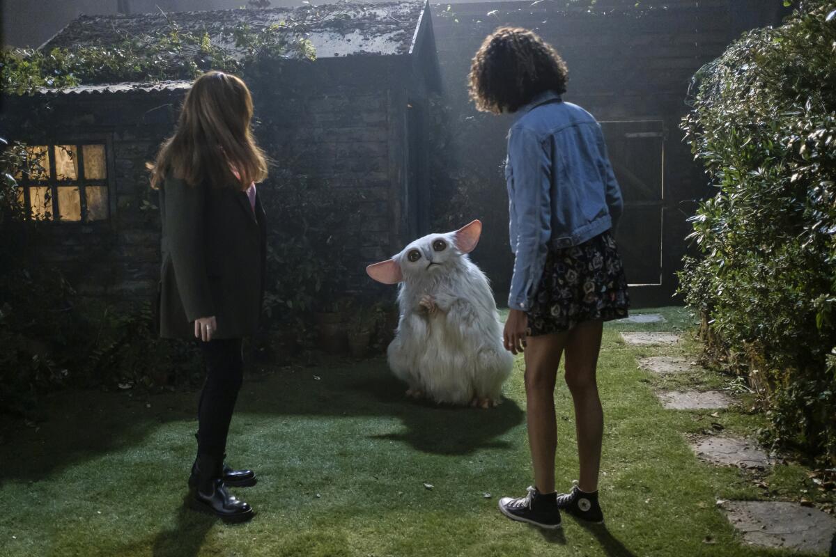Donna Noble und Rose betrachten einen weißen pelzigen Außerirdischen, der in einem Garten mit einer Hütte im Hintergrund steht.