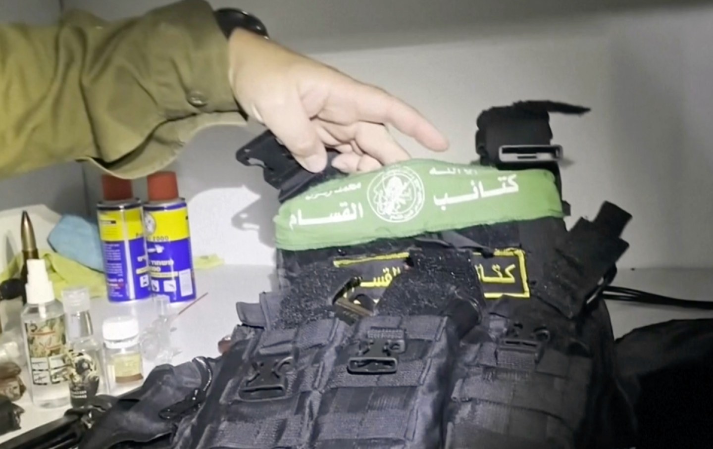 Ein Arm im grünen Hemd hält eine kugelsichere Weste mit Hamas-Insignien hoch