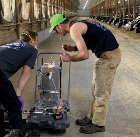 Two workers are examining a small-scale thermal catalytic unit in a barn filled with cows at Drumgoon Dairy in South Dakota.