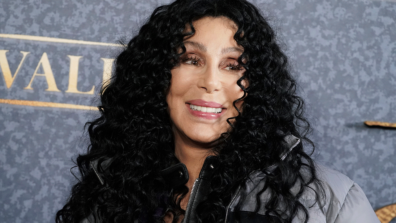 Cher mit lockigem Haar lächelt auf dem Teppich und schaut zur Seite