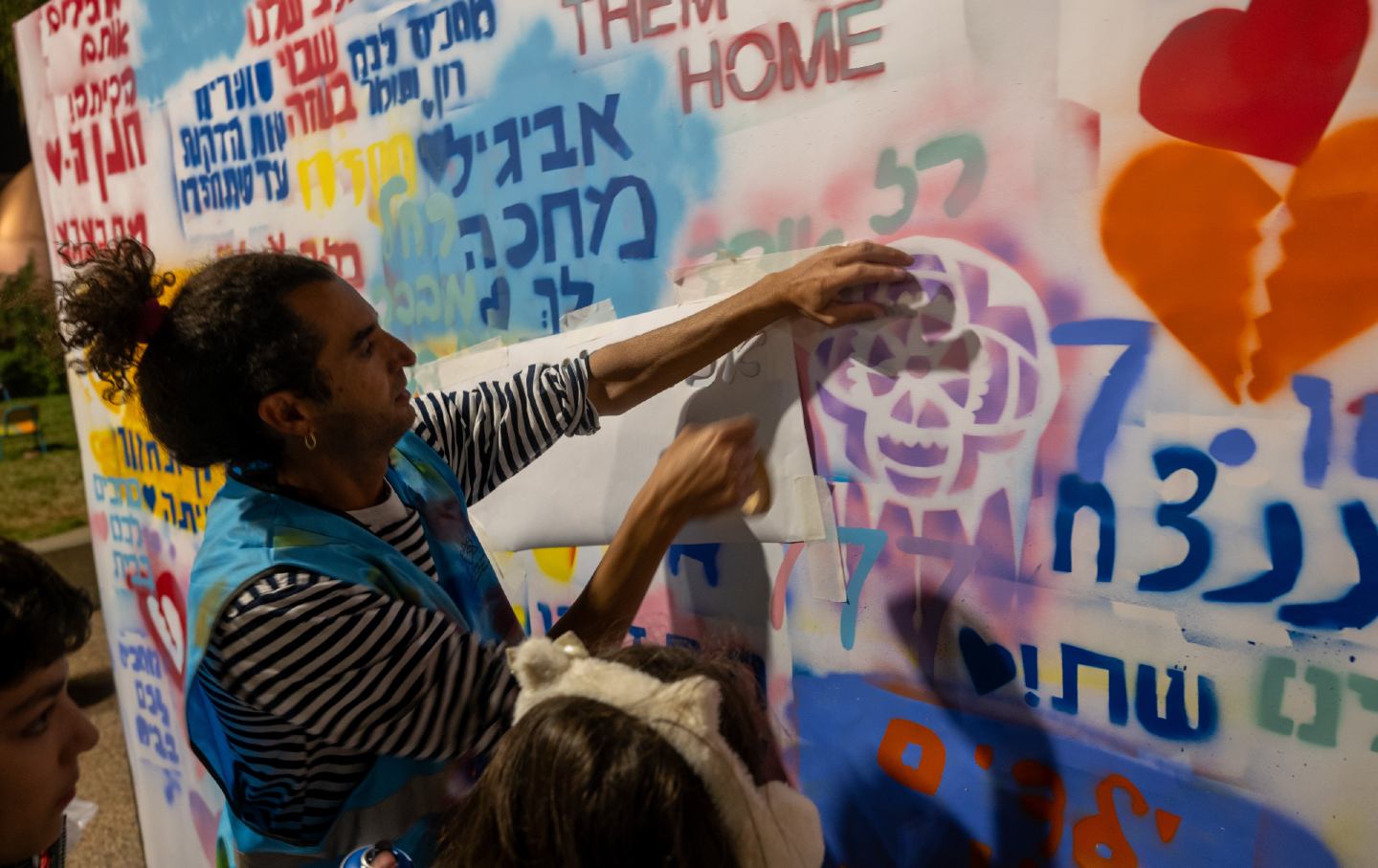 Ein Erwachsener mit zwei Kindern klebt Papier an eine mit Graffiti bedeckte Wand