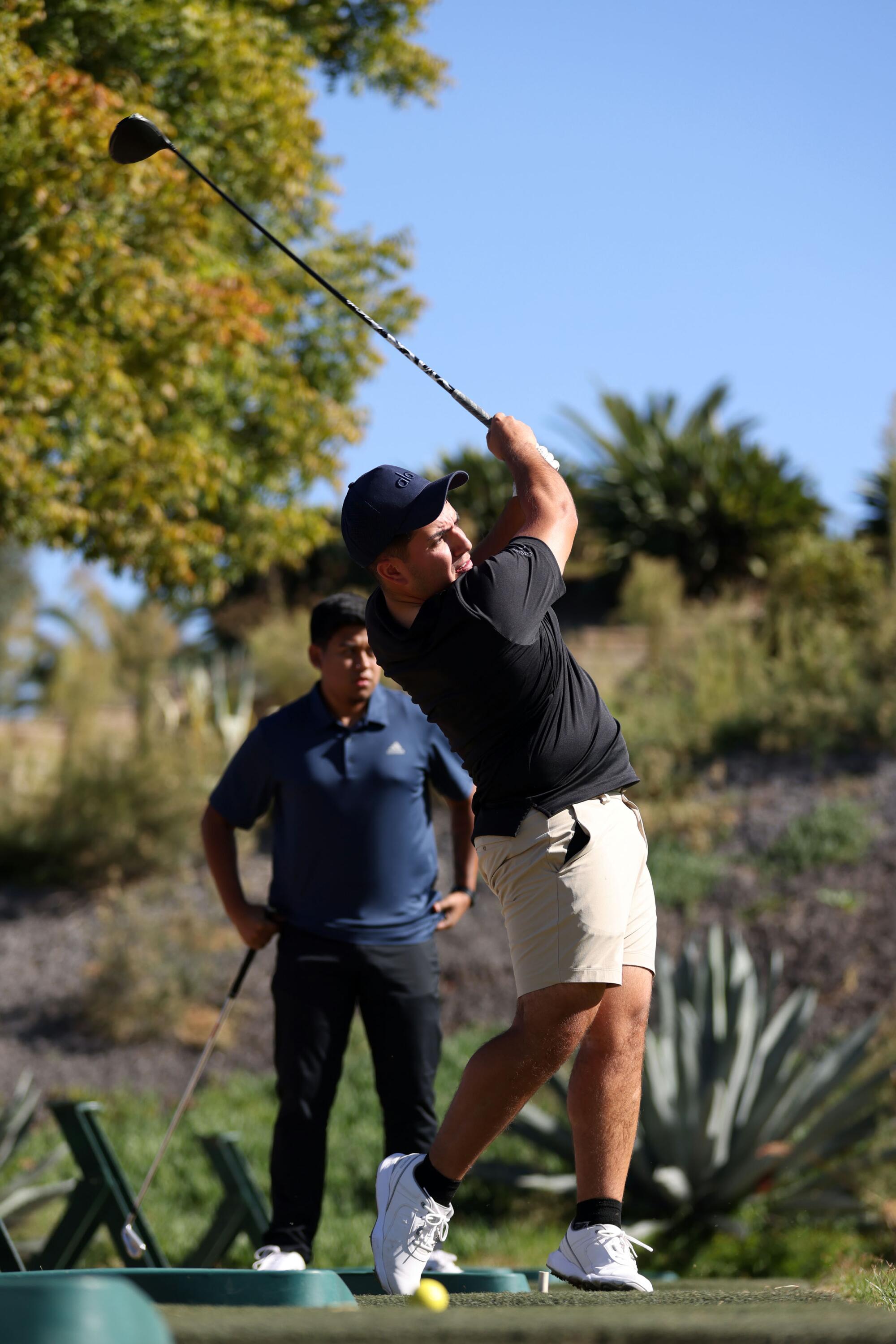 Pedro Tovar von Eslabón Armado schlägt auf einem Golfplatz ab, während er ein schwarzes Hemd und weiße Shorts trägt.