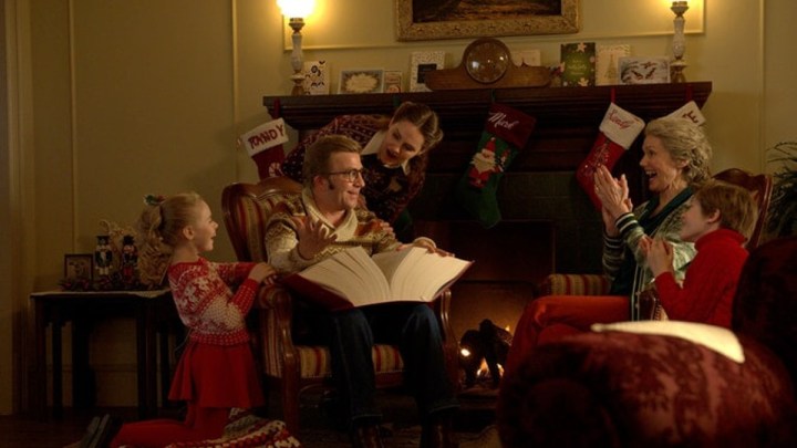 Eine Familie sitzt um ein Feuer und liest ein Buch in einer Szene aus A Christmas Story Christmas.