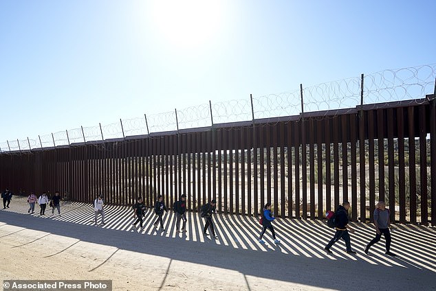 A group of people, including many from China, walk along the wall after crossing the border with Mexico to seek asylum, October 24 near Jacumba, California