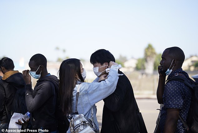 A couple from China adjust their masks as they wait to board a bus to the airport after crossing the border and being dropped off by Border Patrol agents at a transit center in San Diego