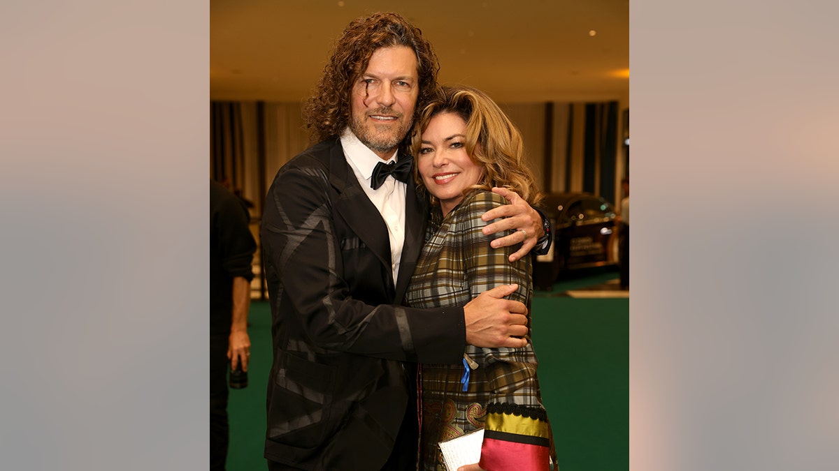 Frédéric Thiébaud in einer gemusterten schwarzen Anzugjacke hält seine Frau Shania Twain in einer grün karierten Jacke fest