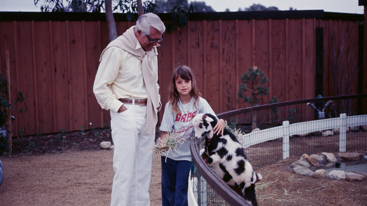 Cary Grant beobachtet seine Tochter Jennifer, wie sie auf einer Farm eine Ziege hält