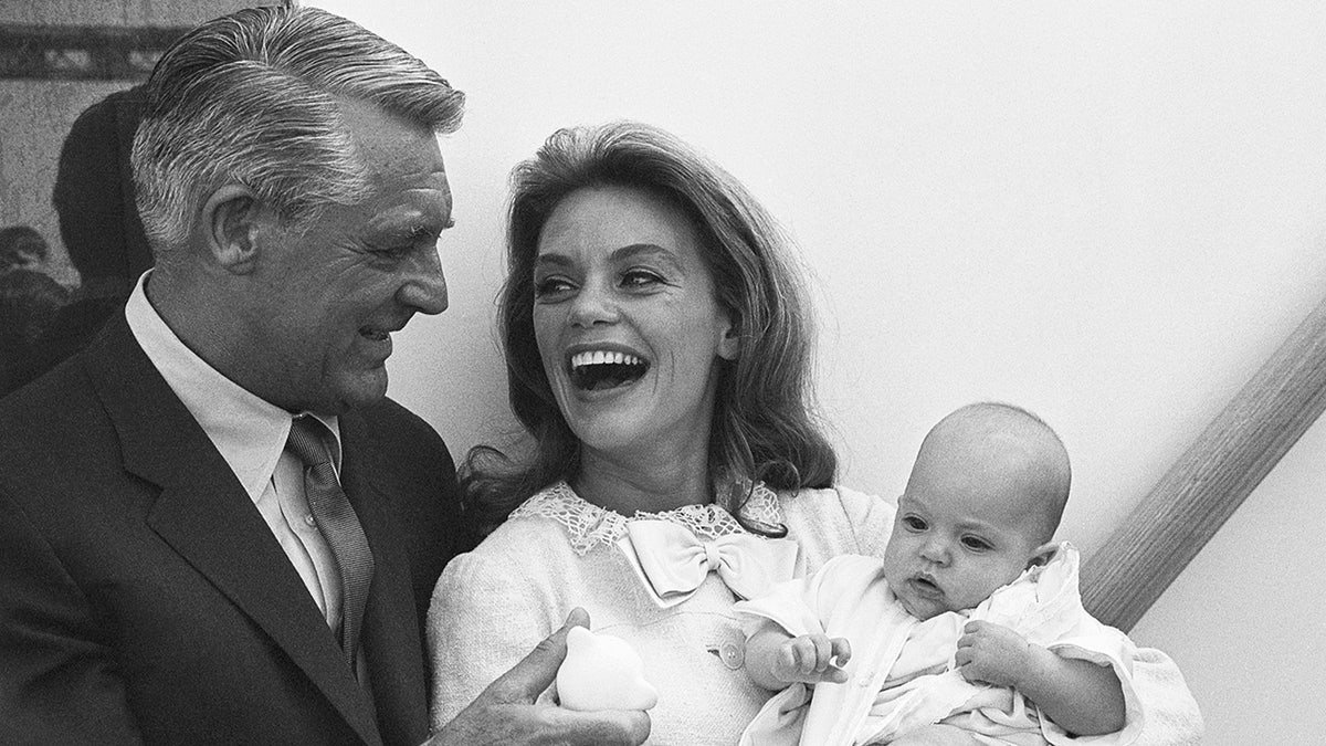 Cary Grant und Dyan Cannon lachen miteinander, während Dyan Cannon ihr Baby Jennifer Grant in den Armen hält