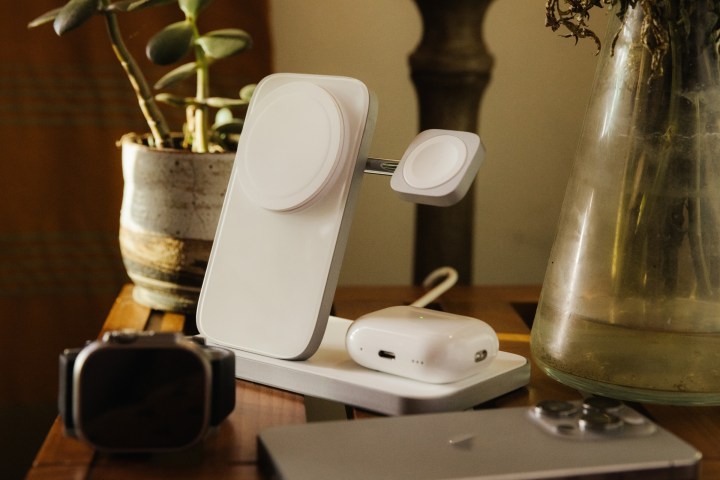 Silberner Nomad Stand One Max iPhone-Ladeständer auf dem Tisch, davor liegen AirPods Pro, iPhone und Apple Watch.
