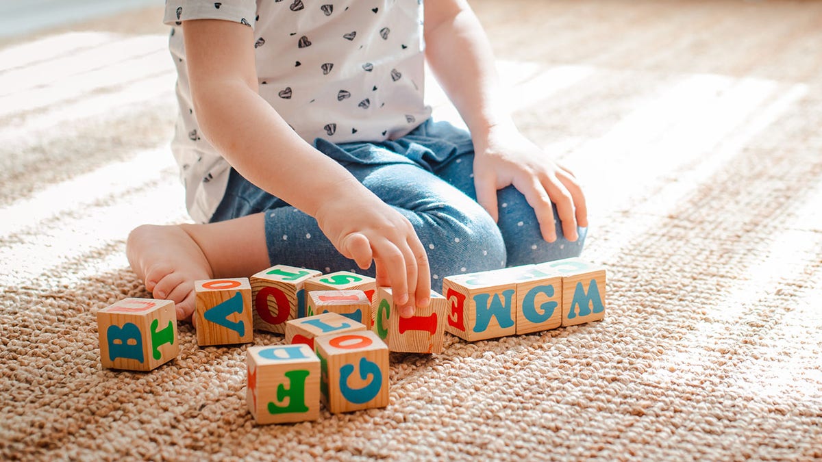 Kind spielt mit Holzwürfeln mit bunten Buchstaben