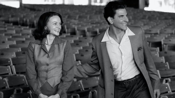 Carey Mulligan und Bradley Cooper als Felicia Montealegre und Leonard Bernstein lächeln, während sie in Maestro in die gleiche Richtung schauen.
