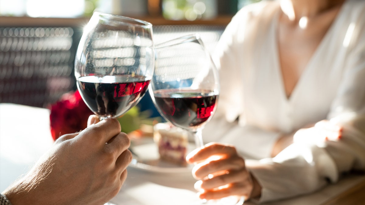 Ein Mann und eine Frau stoßen mit Gläsern Rotwein an.
