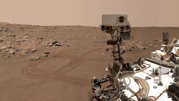 Eine felsige, rostfarbene Landschaft umgibt den Marsrover Perseverance der NASA, der auf Marsboden sitzt.