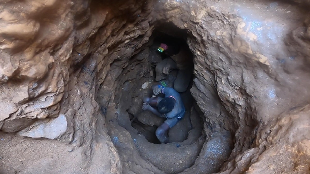 Junge in blauem Hemd und Shorts und eine weitere Person graben in einer Mine nach Kobalt in der Demokratischen Republik Kongo