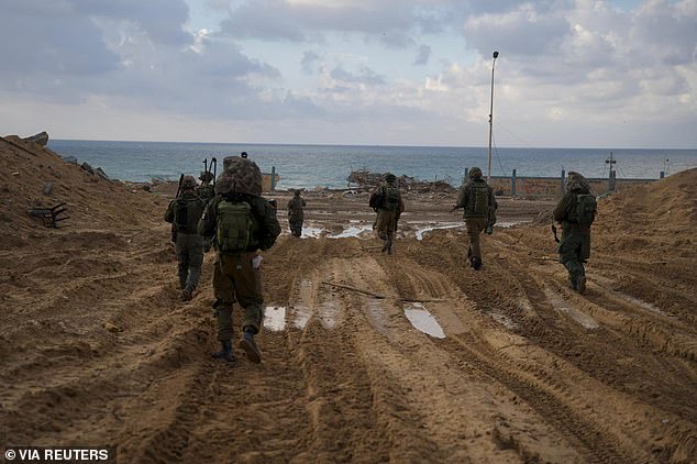 Israeli soldiers walk over tank tracks on a beach in the Gaza Strip as they continue operations