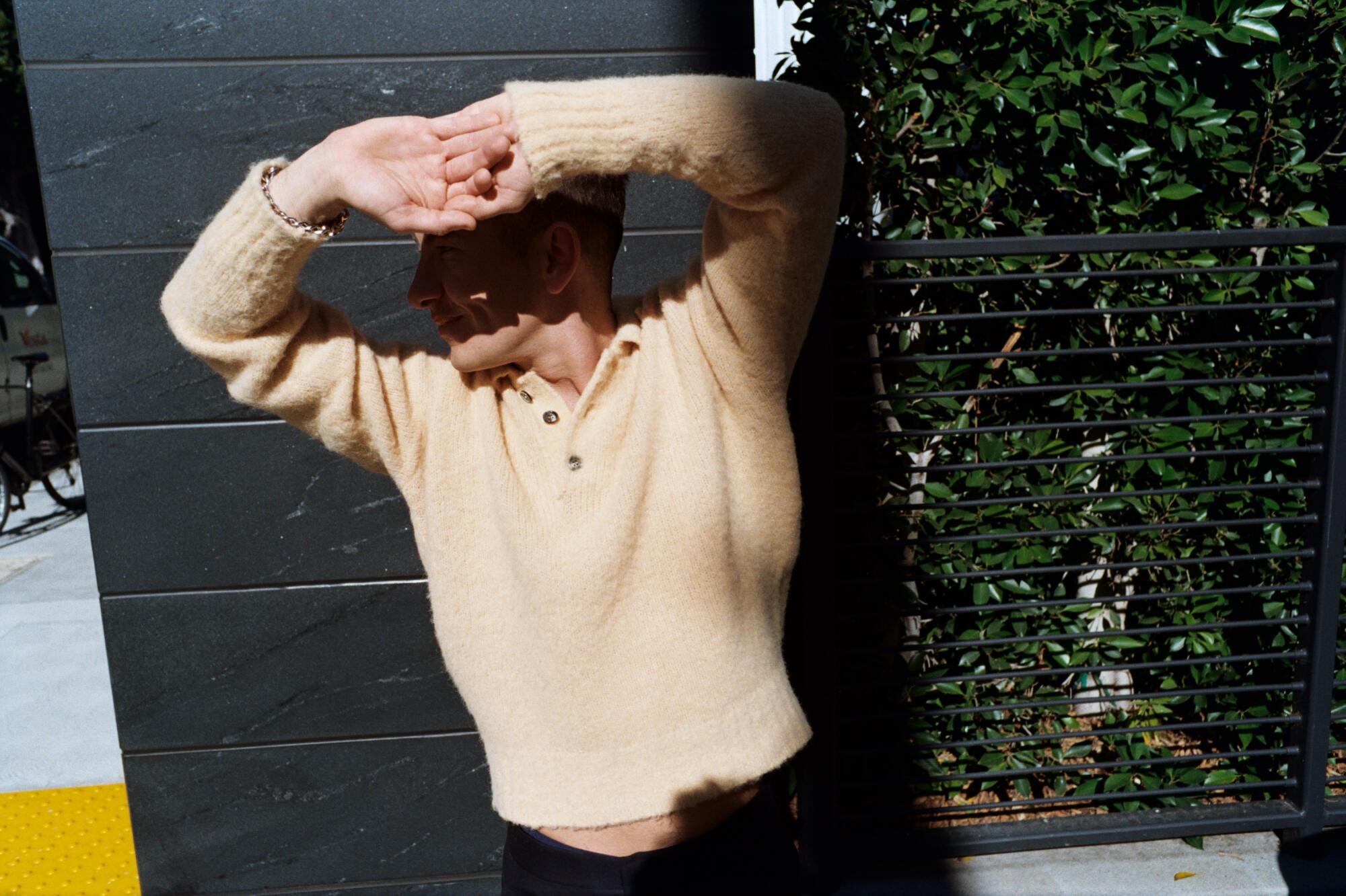 Ein Mann in einem braunen Pullover schützt seine Augen mit seinen Händen vor der Sonne und wirft einen dunklen Schatten auf sein Gesicht.
