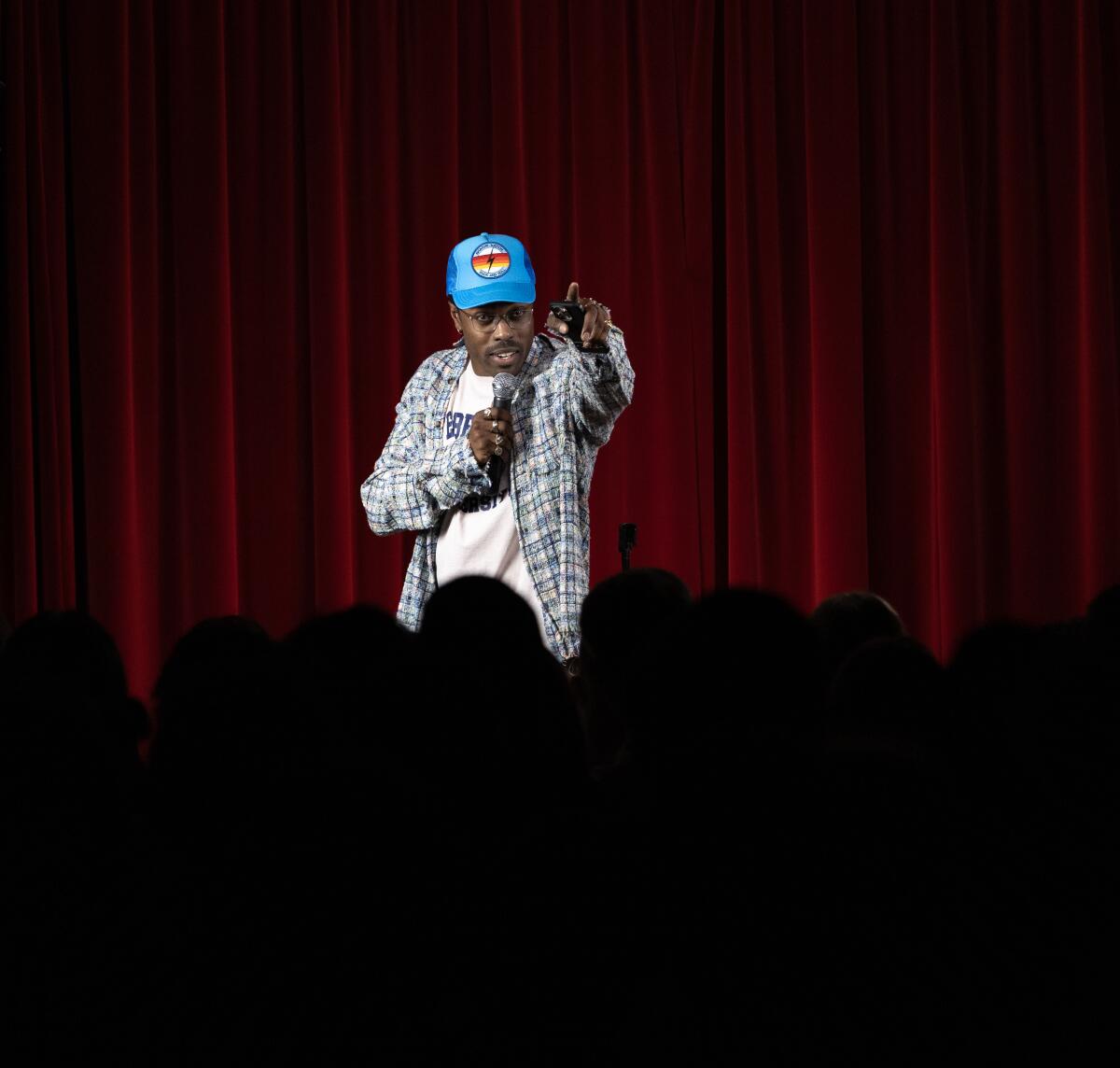 Ein Mann mit blauer Baseballkappe auf der Bühne hält mit einer Hand ein Mikrofon und gestikuliert mit der anderen