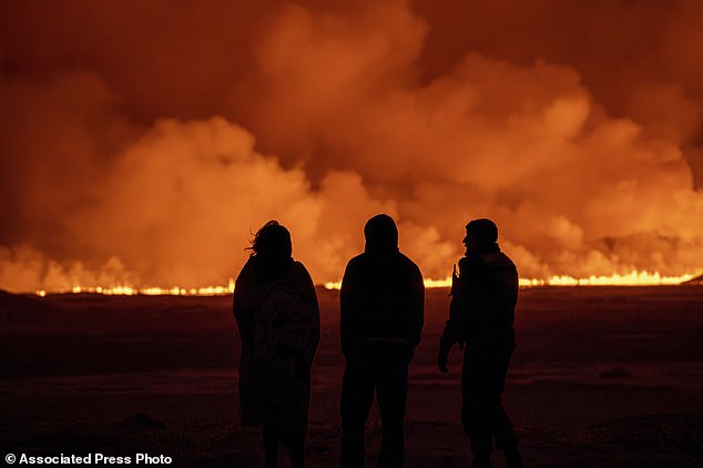 Menschen beobachten, wie der Nachthimmel durch den Ausbruch eines Vulkans in Grindavik auf der isländischen Halbinsel Reykjanes am Montag, 18. Dezember 2023, erleuchtet wird. (AP Photo/Marco Di Marco)