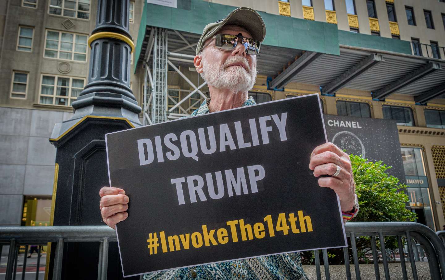 Ein Demonstrant steht vor dem Trump Tower in Manhattan und fordert, dass die Regierungen der Bundesstaaten den ehemaligen Präsidenten Trump gemäß dem 14. Verfassungszusatz von der Teilnahme an Wahlen im Jahr 2024 ausschließen.