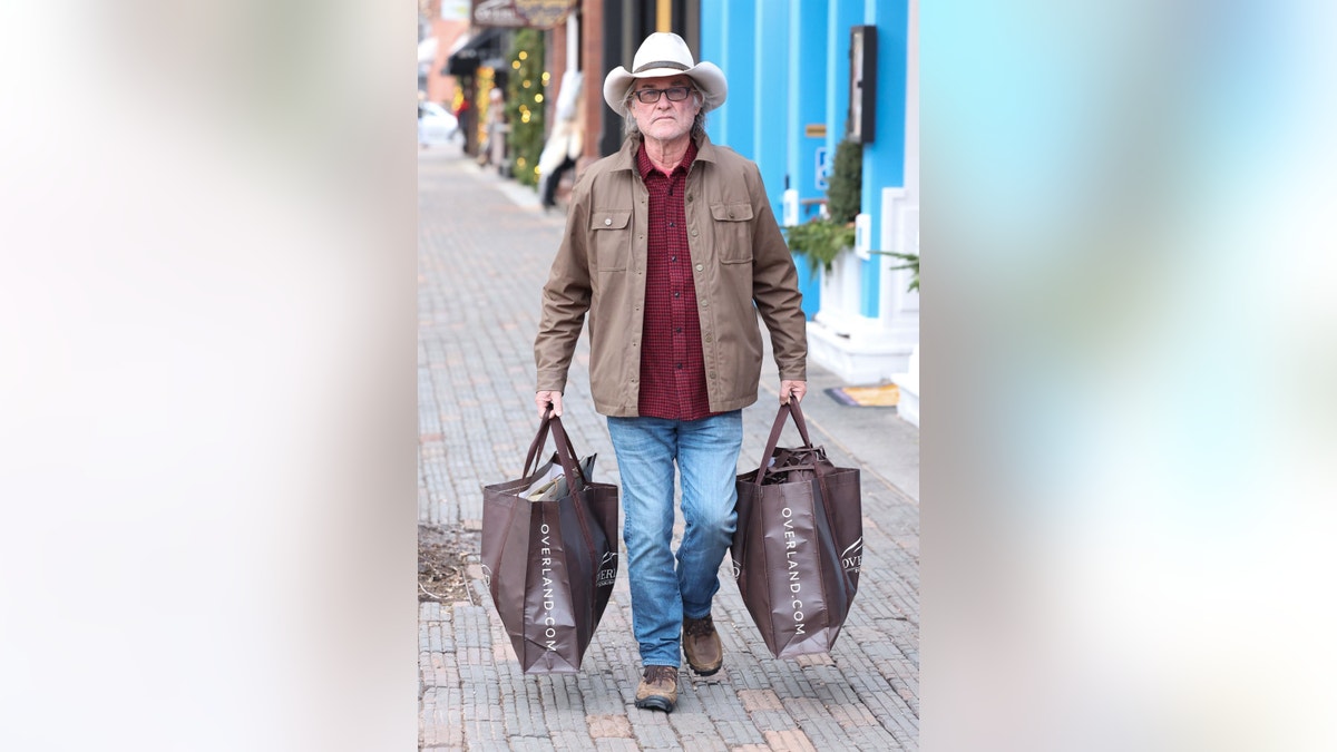 Kurt Russell läuft in Espen den Bürgersteig entlang und trägt zwei große Einkaufstüten
