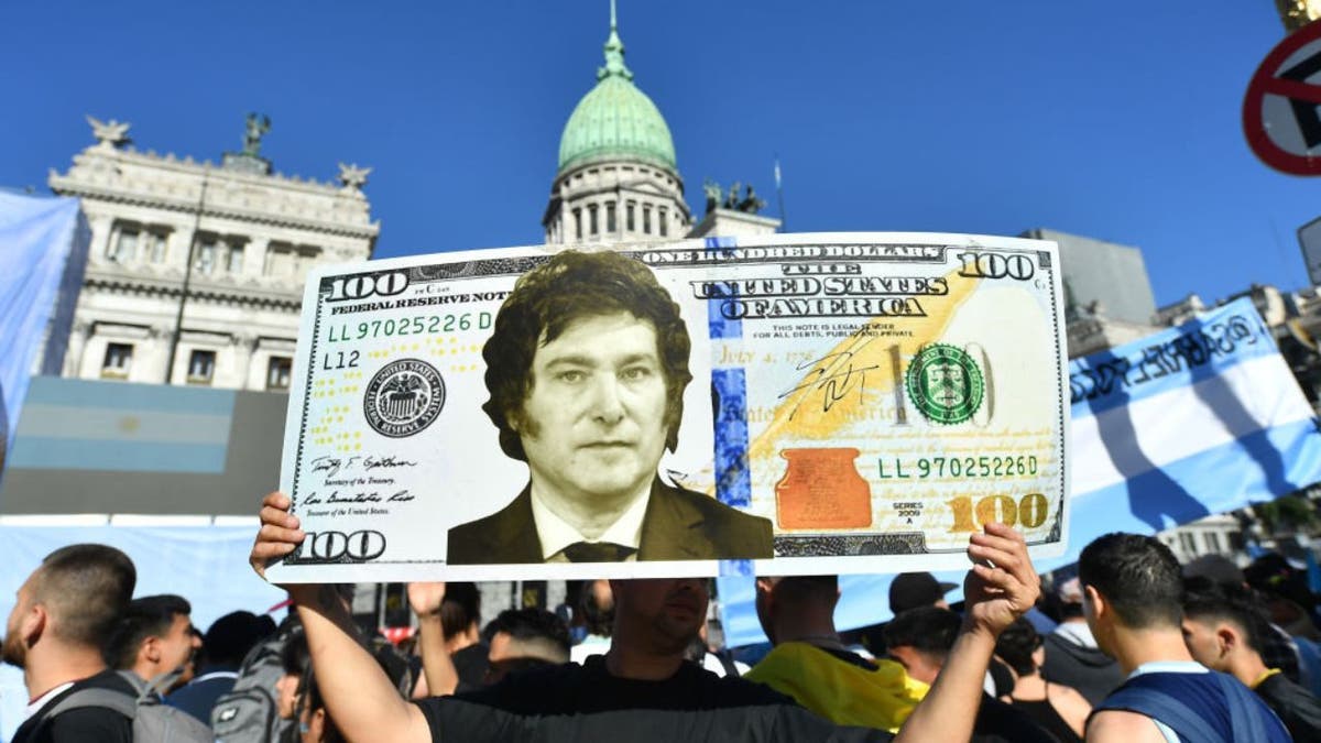 Ein Mann hält zusammen mit dem argentinischen Präsidenten Javier Milei ein riesiges US-Dollar-Zeichen hoch