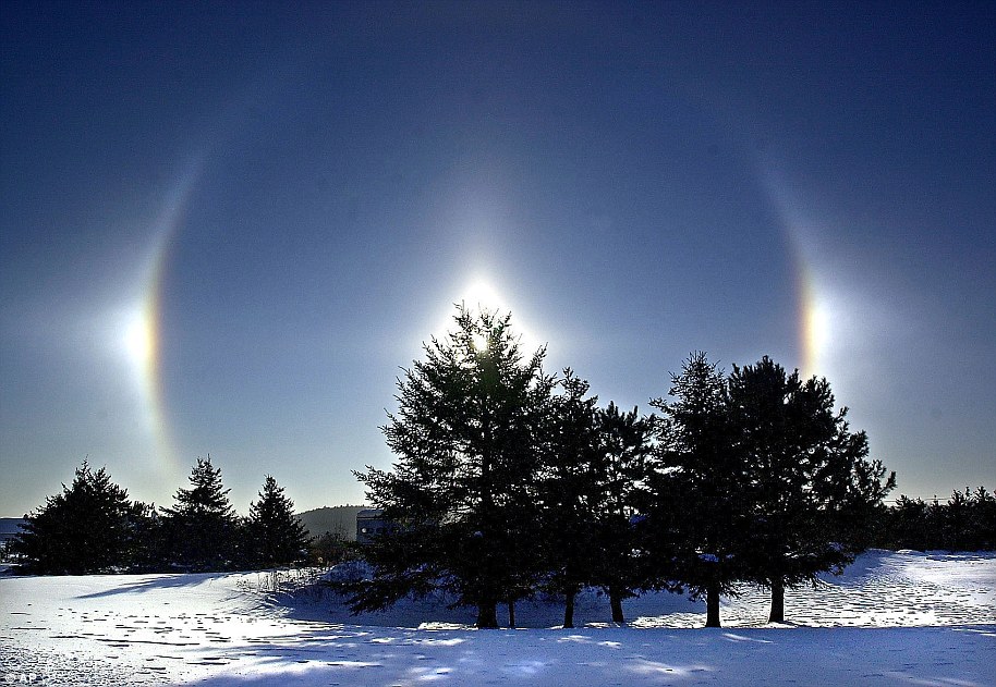 Sundogs oder Parhelia werden über einem schneebedeckten Feld in Duluth gesehen.  Sundogs, wegen der hellen Flecken auf beiden Seiten der Sonne auch Scheinsonnen genannt, entstehen, wenn das Licht der Sonne in der Nähe des Horizonts von Eiskristallen in der Atmosphäre gebrochen wird