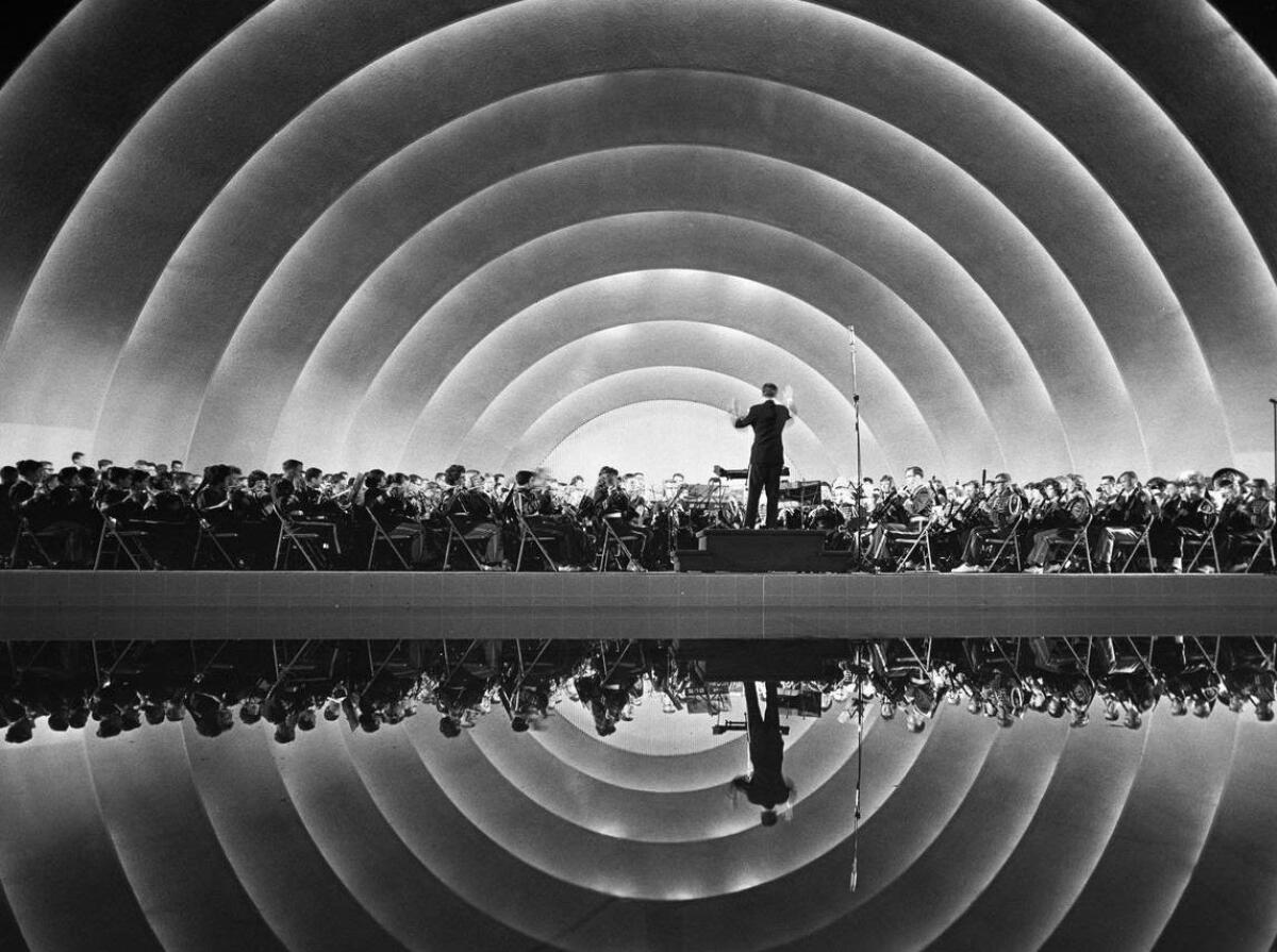 Ein Dirigent leitet ein Orchester im Hollywood Bowl, auf einem Schwarz-Weiß-Foto aus der Sicht des Publikums.
