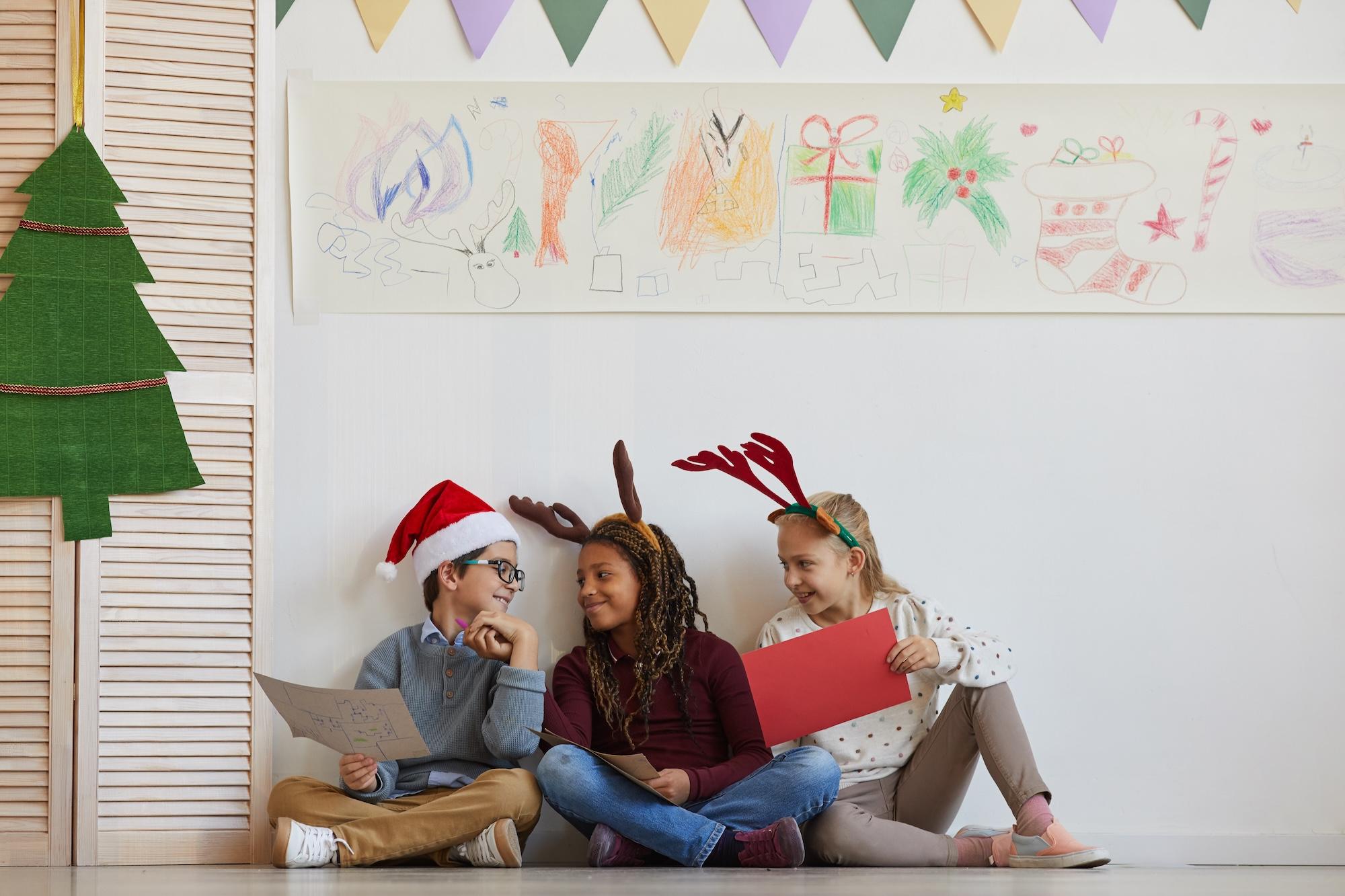 Drei Kinder sitzen während eines Weihnachtskunstkurses auf dem Boden und halten Bilder in der Hand 