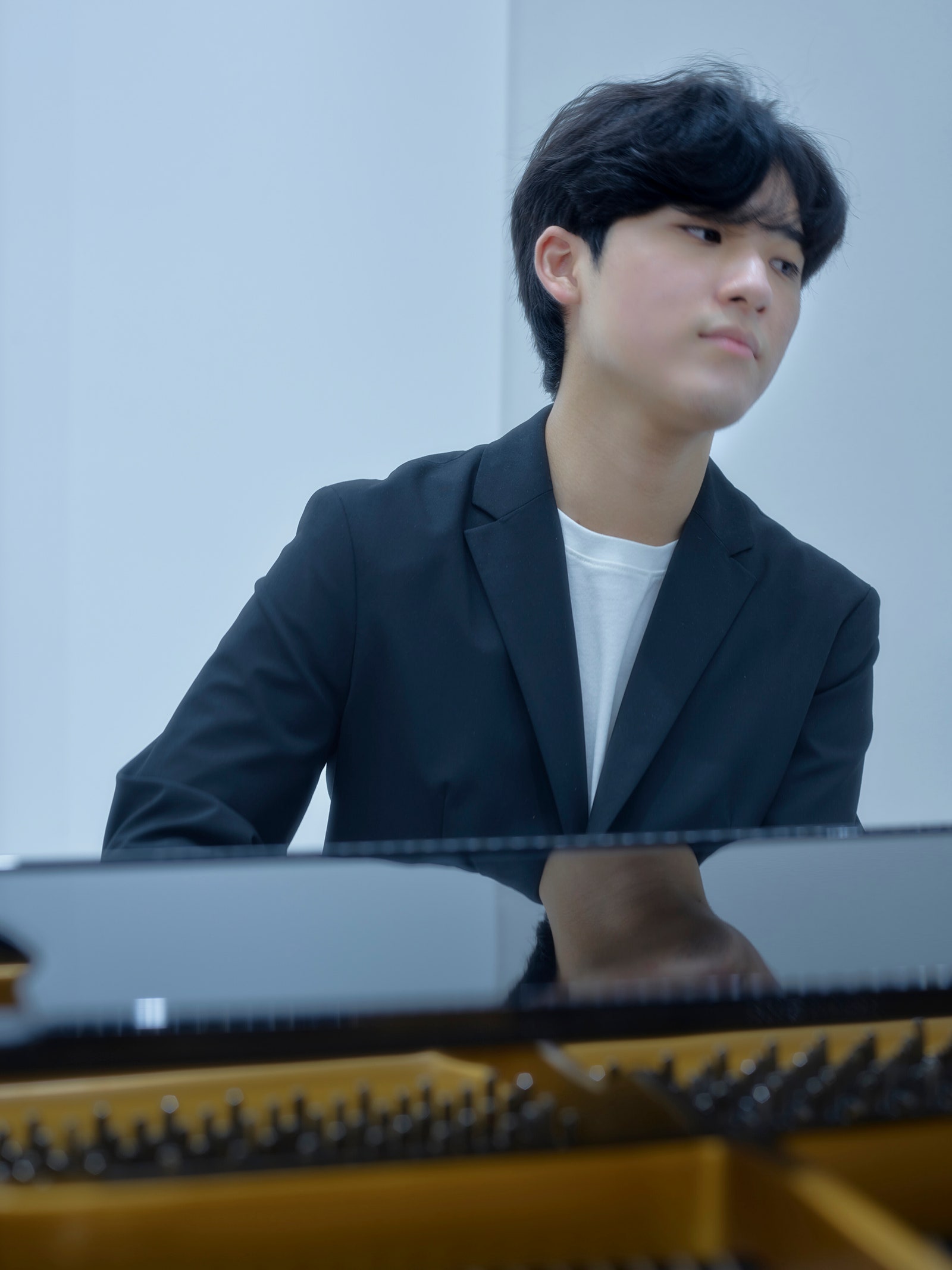 Pianist Yunchan Lim playing a piano wearing a dark blazer and a white tshirt