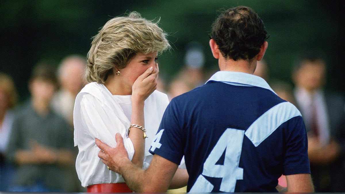 Prinzessin Diana bedeckt ihren Mund, während Prinz Charles sie anstarrt