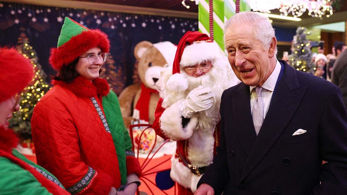 König Charles lächelt neben dem Weihnachtsmann und seinen Elfen