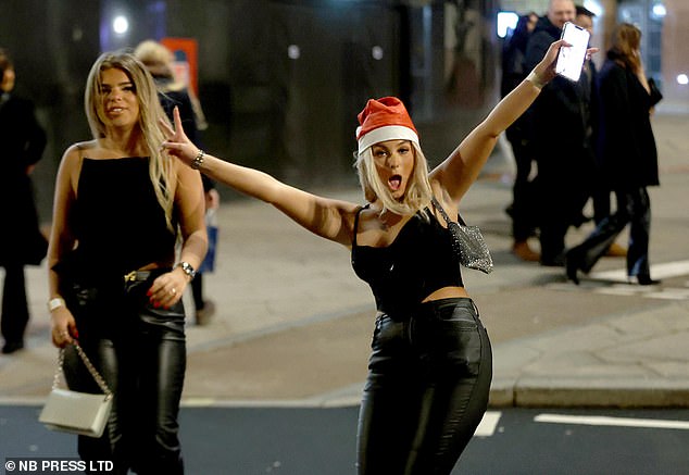 Zwei Frauen mit Weihnachtsmützen und ohne Jacken gehen im kühlen Leeds auf die Straße