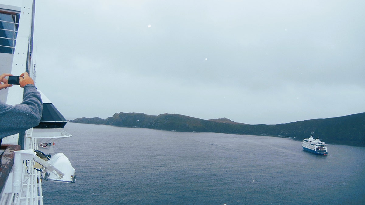 Person, die ein Foto von Kap Hoorn, Chile, macht, während in der Ferne ein Schiff vorbeifährt