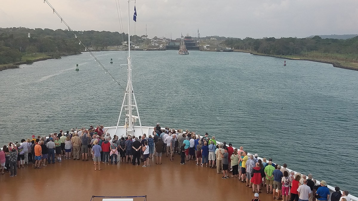 Menschen stehen daneben und beobachten, wie sich ein Kreuzfahrtschiff der Einfahrt in den Panamakanal nähert